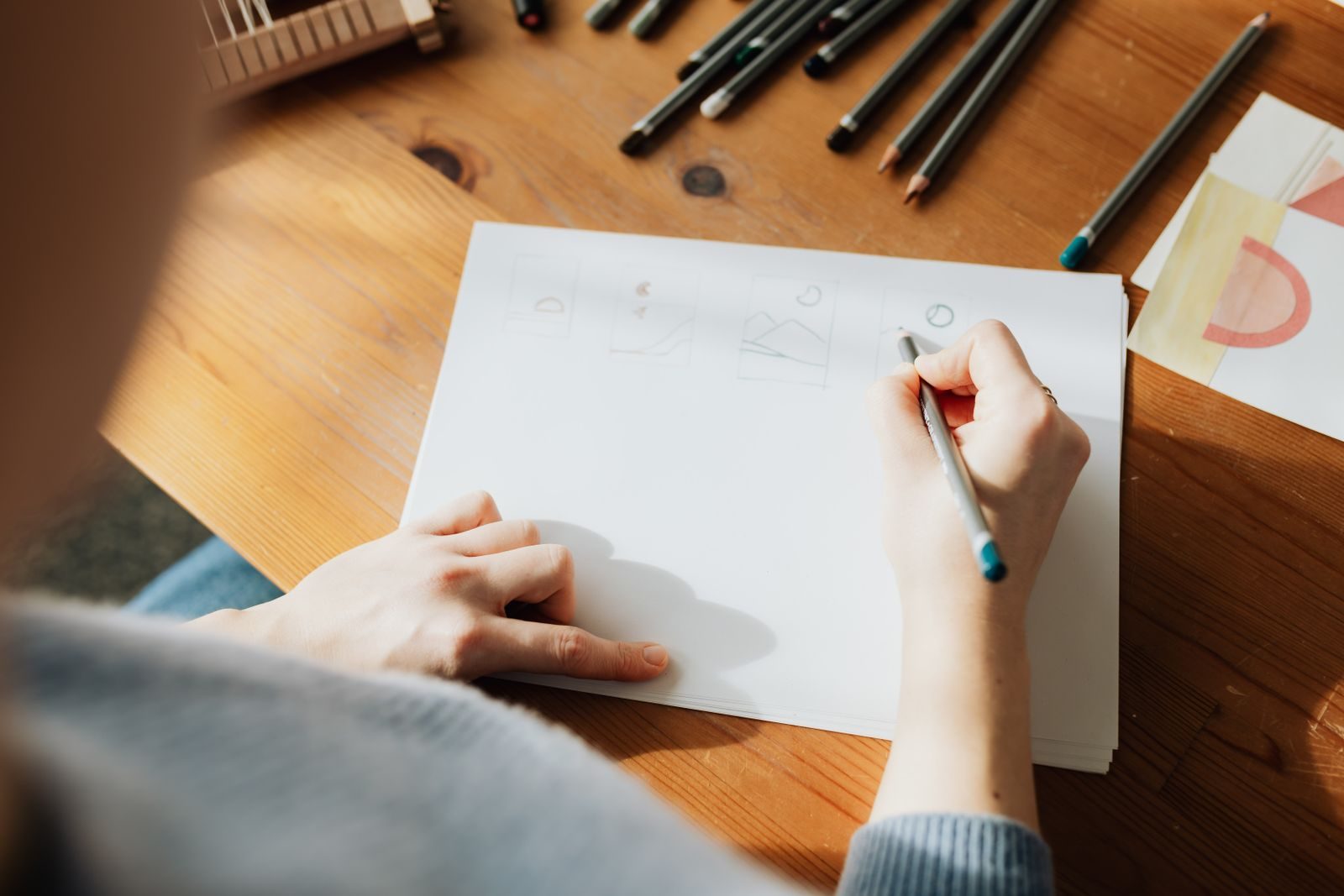 An inventor's worktable seen from above, with an open notebook of hand sketches, a marked-up document, and a coffee cup in morning light.